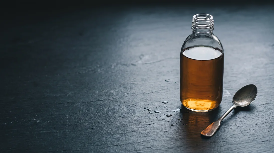 Apple cider vinegar in a glass bottle beside a spoon, the active ingredient behind LipoJelly gummies